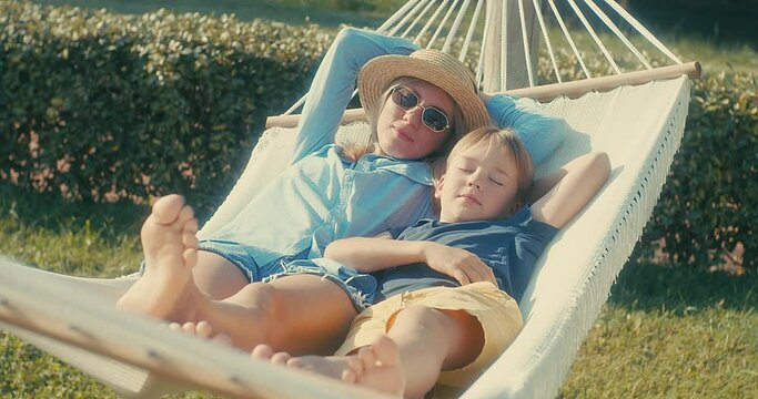 Family fun outdoors, mother and son is resting and using smartphone in hammock in garden, in sunny summer day. Health care, authenticity, sense of balance and calmness. Spend free time. Fresh air.	