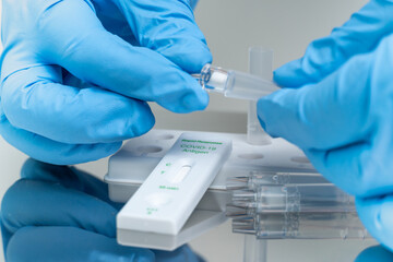 Person in blue gloves performs COVID-19 rapid test at home using personal home test kit for in...