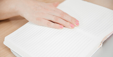 Close up of a woman's hands writing in a notepad placed on a wooden table, home office and work concept, plans and thoughts