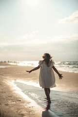 Fototapeta na wymiar Girl playing on the beach in water wearing summer dress