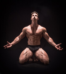 Handsome shirtless muscular man on his knees on dark background