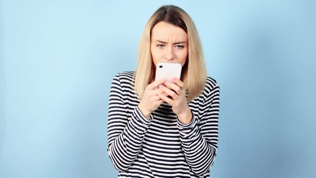 Anxious paranoid young woman nervously typing on a smartphone, scrolling through news or social media feed looking around so that no one is spying on isolated blue background Phone addiction concept