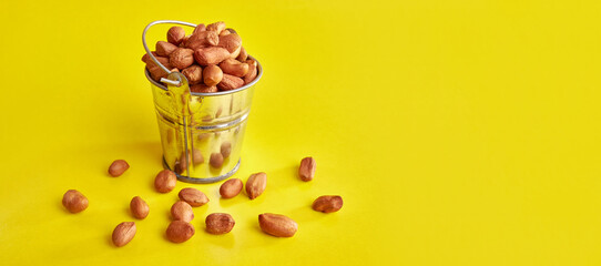 A small metal bucket filled with raw peanuts on a yellow background.