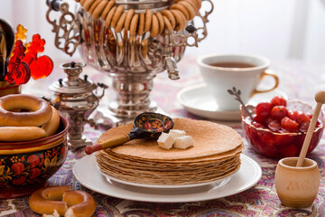 Russian traditions. Russian holiday Maslenitsa. Still life with a cup of tea, a stack of pancakes, sour cream, honey, cubes of butter, bagels, dried fruits, caramel cockerel and samovars.