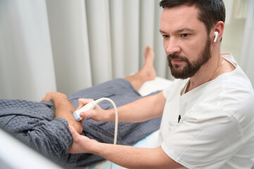 Obraz premium Concentrated therapist doing an ultrasonography of person elbow