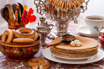 Russian traditions. Russian holiday Maslenitsa. Still life with a cup of tea, a stack of pancakes, sour cream, honey, cubes of butter, bagels, dried fruits, caramel cockerel and samovars.