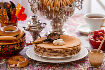 Russian traditions. Russian holiday Maslenitsa. Still life with a cup of tea, a stack of pancakes, sour cream, honey, cubes of butter, bagels, dried fruits, caramel cockerel and samovars.