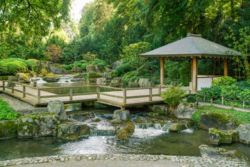 Fototapeta na wymiar Wooden gazebo and small waterfall in japanese gardenin Botanical garden in Augsburg