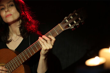 Obraz premium Beautiful Woman playing guitar isolated on black background with candles, copy space. Studio light. Music. Guitar classic