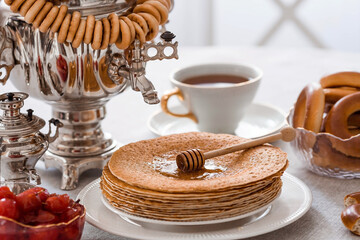 Russian traditions. Russian holiday Maslenitsa. Still life with a cup of tea, a stack of pancakes, sour cream, honey, cubes of butter, bagels, dried fruits, caramel cockerel and samovars.