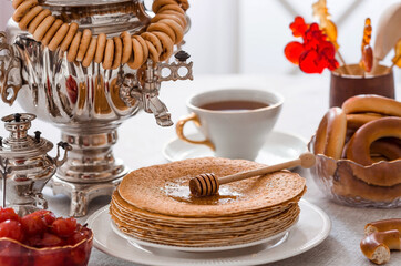 Russian traditions. Russian holiday Maslenitsa. Still life with a cup of tea, a stack of pancakes, sour cream, honey, cubes of butter, bagels, dried fruits, caramel cockerel and samovars.