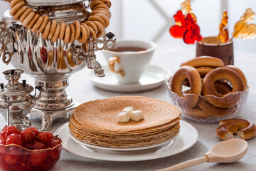Russian traditions. Russian holiday Maslenitsa. Still life with a cup of tea, a stack of pancakes, sour cream, honey, cubes of butter, bagels, dried fruits, caramel cockerel and samovars.