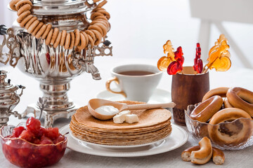 Russian traditions. Russian holiday Maslenitsa. Still life with a cup of tea, a stack of pancakes, sour cream, honey, cubes of butter, bagels, dried fruits, caramel cockerel and samovars.