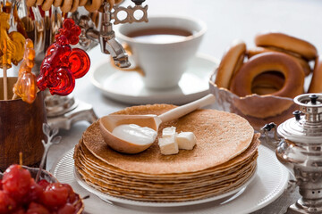 Russian traditions. Russian holiday Maslenitsa. Still life with a cup of tea, a stack of pancakes, sour cream, honey, cubes of butter, bagels, dried fruits, caramel cockerel and samovars.