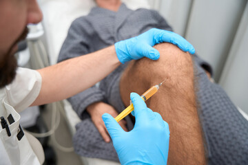 Experienced doctor taking a biopsy sample from man knee