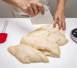 Closeup chef using plastic cutter cut the organic dough after kneading on the white surface. Baker making homemade loaf of bread and pastry. Preparation of fresh pasta, pizza raw wheat ingredient.