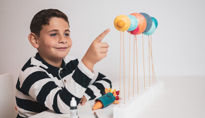 A child makes the planets of the solar system out of cork for a school project. The little boy points to the planets to study them. Concept of astronomy for children.