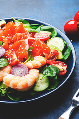 Salmon salad for ketogenic diet with shrimp, avocado, spinach, cucumber, tomato, cashew nuts, sesame. Low-carbohydrate lunch rich in healthy fats. Blue table background, top view