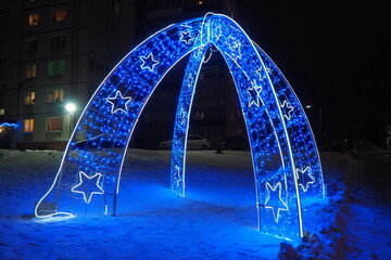 Arch with blue street garlands. Festive background. Blue and white light bulbs as a decoration for the New Year and Christmas night. Street decoration design. Abstract light spots. Star shape