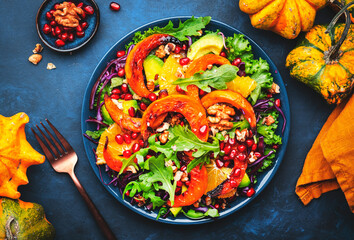 Fresh pumpkin salad with lettuce,  red cabbage, avocado, arugula, pomegranate seeds and nuts. Healthy vegan vegetarian eating, slow comfort food. Blue table background. Top view