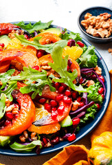 Fresh pumpkin salad with red cabbage, avocado, lettuce, arugula, pomegranate and nuts. Vegan healthy eating, slow comfort food. White table background. Top view