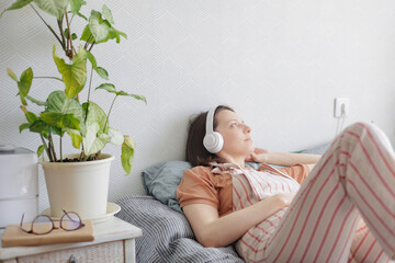 woman listens to music with headphones online from a smartphone at home. young adult woman is lying...