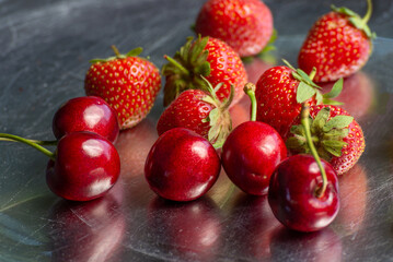 A view of several varieties of fruit and berries scattered on a silver surface, featuring strawberry and cherry.