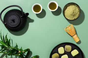 matcha tea with teapot and tea cups on green background with copy space