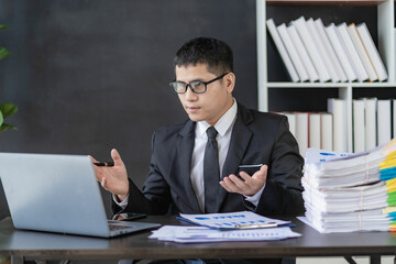 Asian financier doing accounting work in glasses working with documents and laptop Businessman sitting at desk with stacks of papers in office building