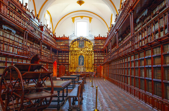 March 17, 2022. Puebla Mexico. Interior view of the Baroque style Palafoxiana Library with two levels of wood carved bookshelves and the golden engraved retable of the Madonna of Trapani.