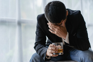Stressed Asian businessman holding glass of whiskey and at desk Alcohol addiction, drunken...