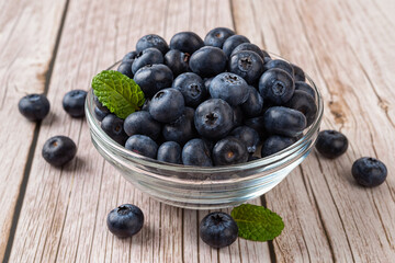 Ripe blueberry in a glass bowl over wooden background. Fresh blueberries for vegetarian dessert. Wild berry for natural antioxidant and healthy eating concept. Vitamin vegan snack.