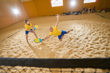 Man is jumping on partner while playing beach tennis