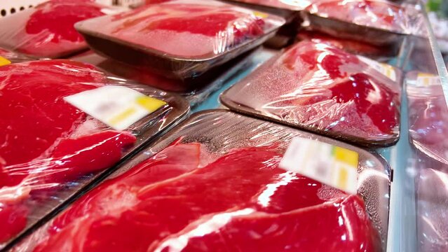 Raw beef fillets or steaks in cling-wrap plastic containers are in a supermarket refrigerator. Close-up shot