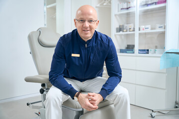 Employee with badge on shirt sits background racks with medical gadgets