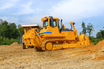 Crawler dozer working on construction site or quarry. Mining machinery moving clay, smoothing gravel surface for new road. Earthmoving, excavations, digging on soils