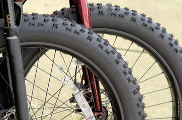 Closeup of nubby back wheels of two off-road bicycles parked at an outdoor facility