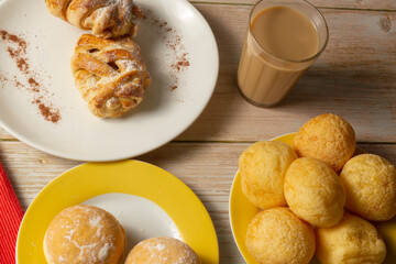 Table with Brazilian snacks. Cheese bread, sweet brioche, coffee with milk, and Berlin ball, a Brazilian donut called 