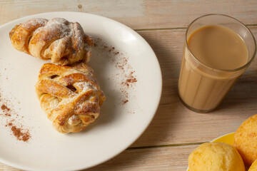 Mini sweet brioches topped with cinnamon powder and grated coconut on a dish and a mug of latte for a breakfast. Top view. selective focus.