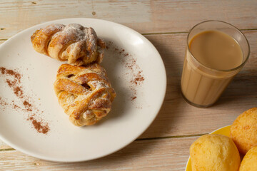 Mini sweet brioches topped with cinnamon powder and grated coconut on a dish and a mug of latte for a breakfast. Top view. selective focus.