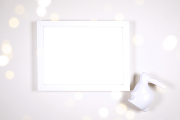 Horizontal artwork wall art picture frame product mockup. Happy Easter theme product mockup. Minimal styling with bunny rabbit against a bokeh party lights background. Negative copy space.
