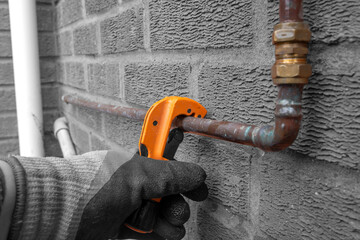 Man cutting copper water pipe with a pipe cutter tool outdoors. Plumbing work concept with selective colour