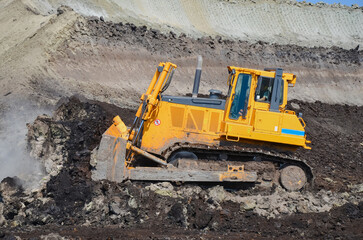 Obraz premium Crawler bulldozer working on construction site or quarry. Mining machinery moving clay, smoothing gravel surface for new road. Earthmoving, excavations, digging on soils