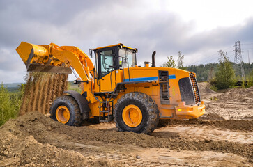 Whell loader working on construction site or quarry. Mining machinery moving clay, smoothing gravel surface for new road. Earthmoving, excavations, digging on soils