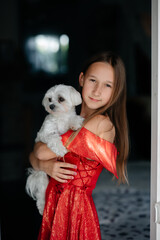 A little girl with loose hair hugs her little white lapdog in the living room of a country house