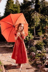 A little girl with loose hair in a red dress with a big red umbrella outside in clear weather