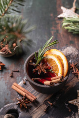 Mulled red wine in ceramic bowl close up with spices, fruits and rosemary on wooden rustic table, dark key. Traditional hot drink at Christmas time and winter