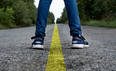 Legs of a guy in jeans and sneakers on an asphalt road with a dividing strip
