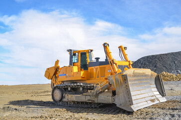 Obraz premium Big crawler dozer working on construction site or quarry. Mining machinery moving clay, smoothing gravel surface for new road. Earthmoving, excavations, digging on soils
