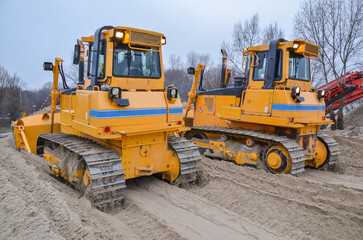 Crawler bulldozers working on construction site or quarry. Mining machinery moving clay, smoothing gravel surface for new road. Earthmoving, excavations, digging on soils